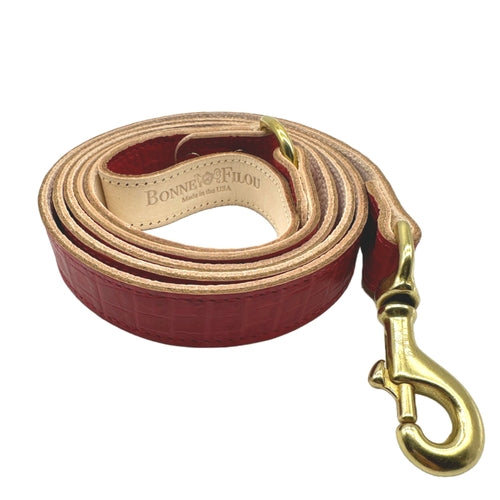Red leather dog leash with gold clasp on a white background
