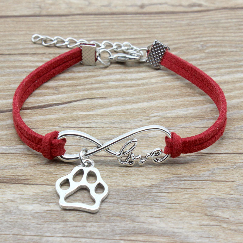 Red bracelet with silver infinity charm and paw print charm on a wooden surface