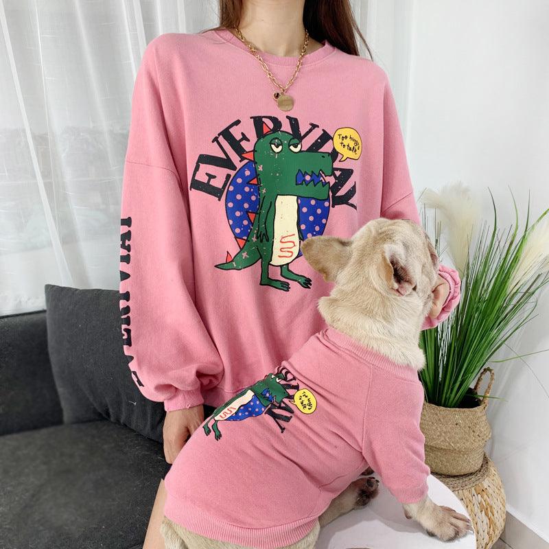 Person wearing a pink sweatshirt with a cartoon design, standing next to a dog in a matching pink outfit.