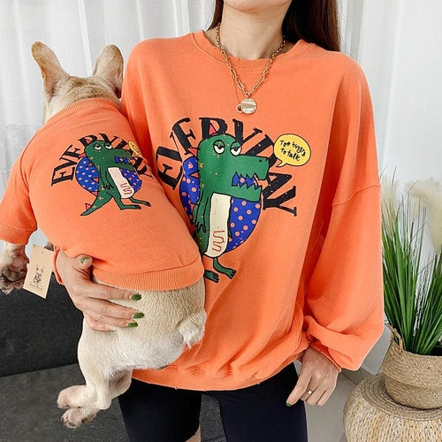 Person and dog wearing matching orange sweatshirts with cartoon frog designs.
