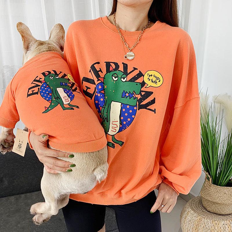 Person wearing an orange sweatshirt with a cartoon frog design, holding a dog also wearing an orange sweatshirt with the same design.