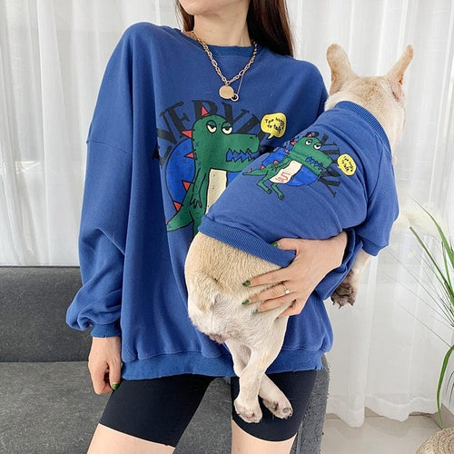Person wearing a blue sweatshirt with cartoon designs, holding a small dog.