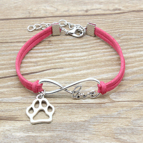 Pink bracelet with silver paw charm and 'love' inscription on a wooden surface