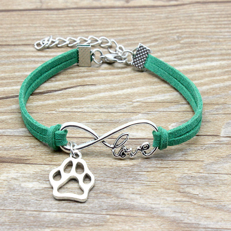 Green bracelet with silver infinity and paw charm on a wooden surface