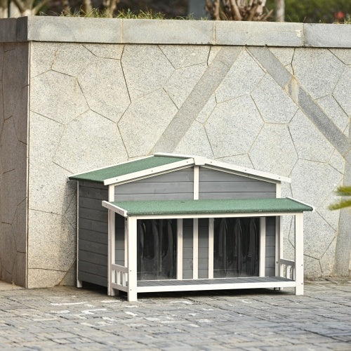 Wooden pet house with green roof against a stone wall.