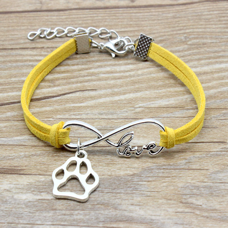 Yellow bracelet with silver paw charm and 'love' inscription on a wooden surface