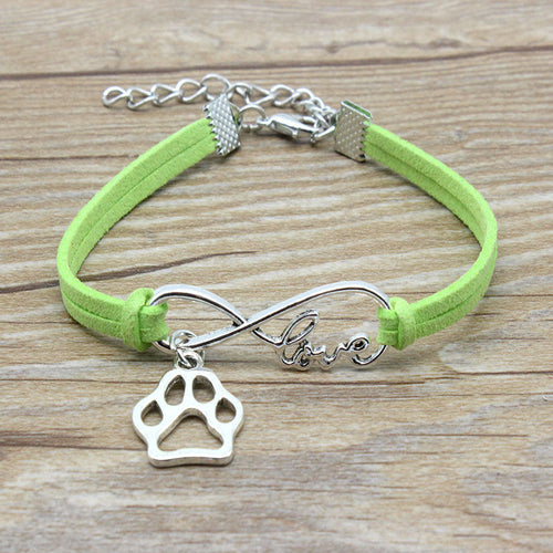 Green bracelet with silver paw charm and 'love' infinity symbol on a wooden surface