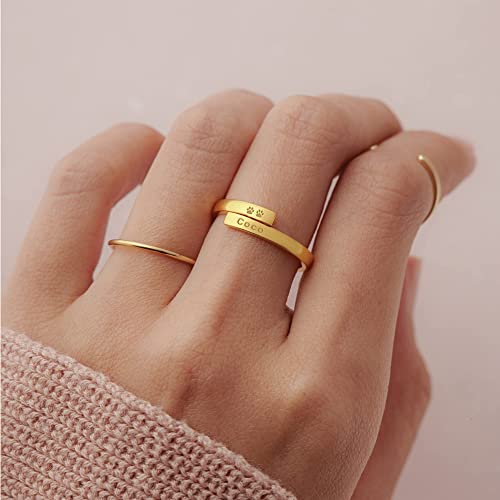 Gold ring with paw print design and engraved text on a hand against a light pink background