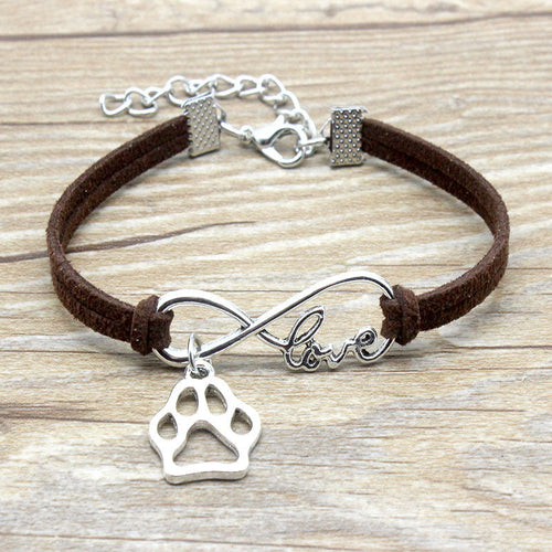 Bracelet with paw charm and 'love' infinity symbol on brown cord, on wooden surface