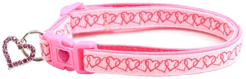 Pink dog collar with heart patterns and a keychain on a white background