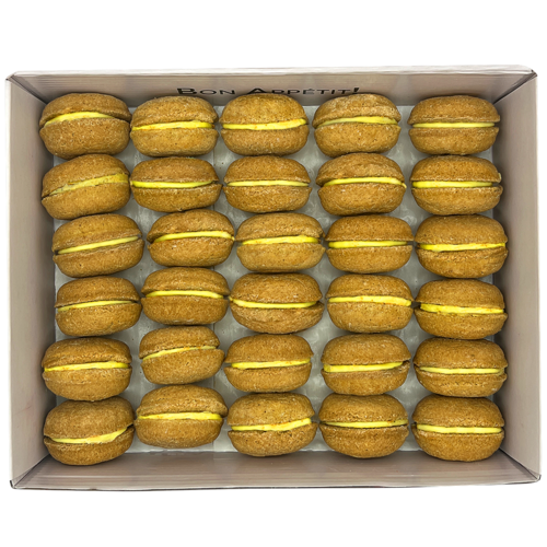Box of yellow macarons with green filling on a white background