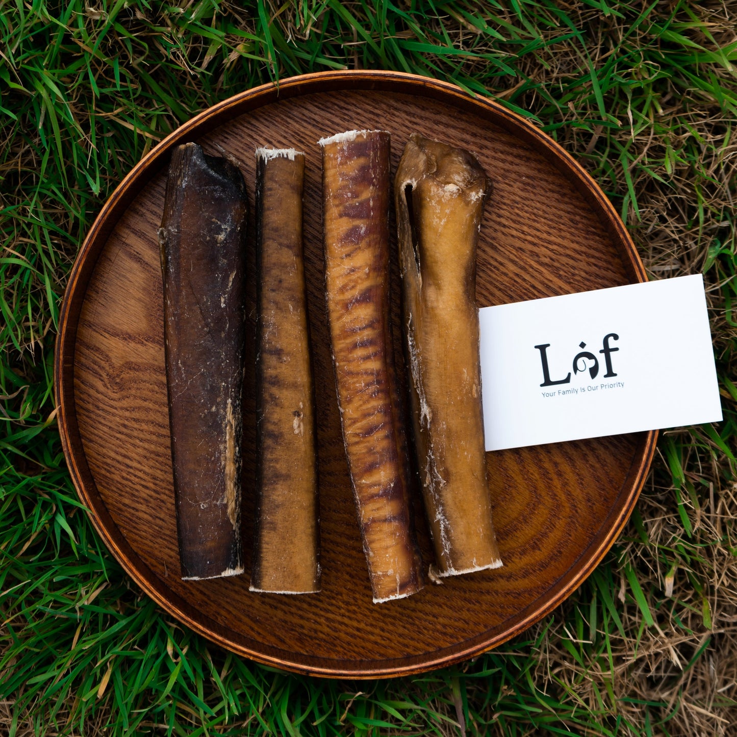 Dog chew bones on a wooden plate with a 'Lof' brand card on grass