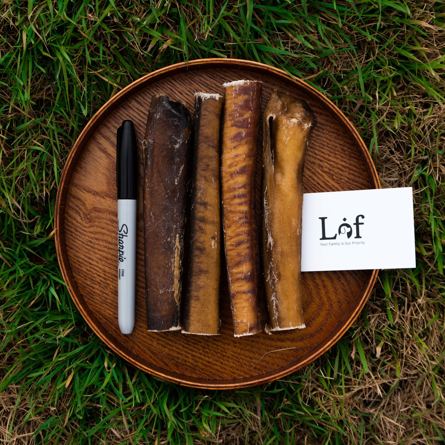 Wooden plate with dog bones and a pen on grass, featuring the brand 'Láf'.