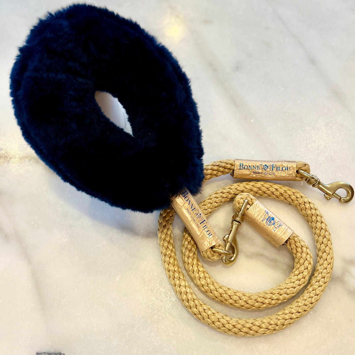 Navy blue fur dog muzzle with a gold braided leash on a white surface