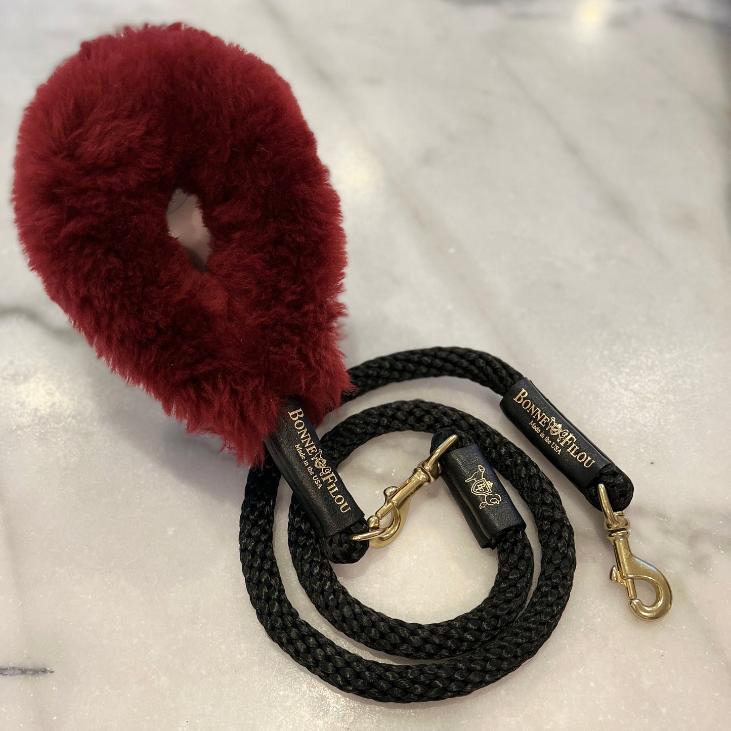 Black dog leash with gold hardware and a red fluffy handle on a white background
