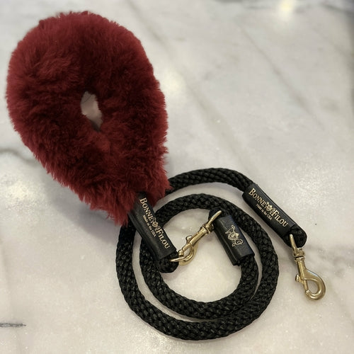 Black dog leash with gold hardware and a red fluffy dog toy on a white background