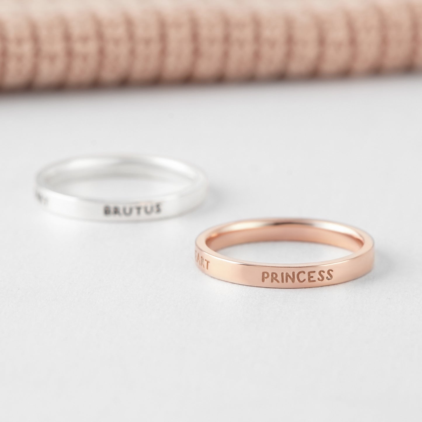 Two rings, one silver and one rose gold, with engraved names on a light background.