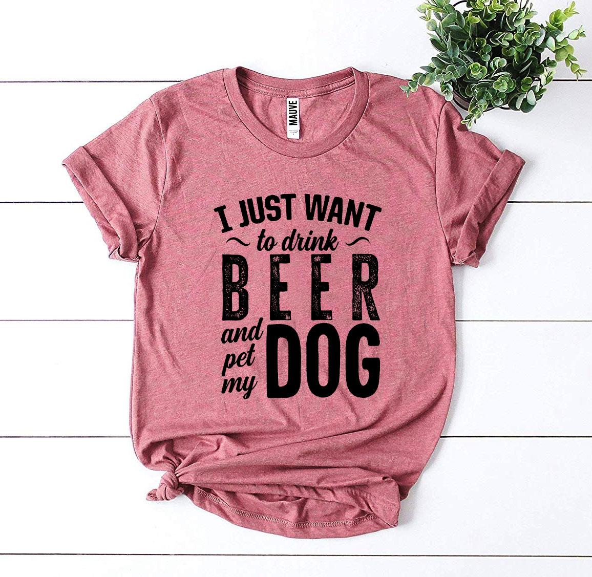 Pink t-shirt with text 'I just want to drink beer and pet my dog' on a white wooden surface.