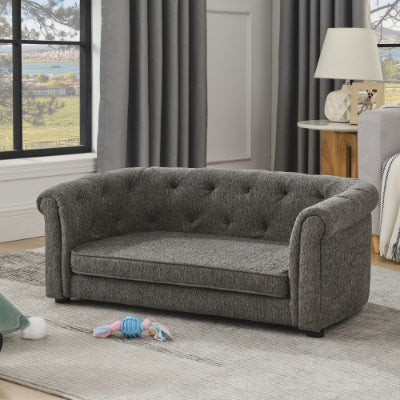 Gray tufted sofa in a living room with curtains and a lamp in the background.