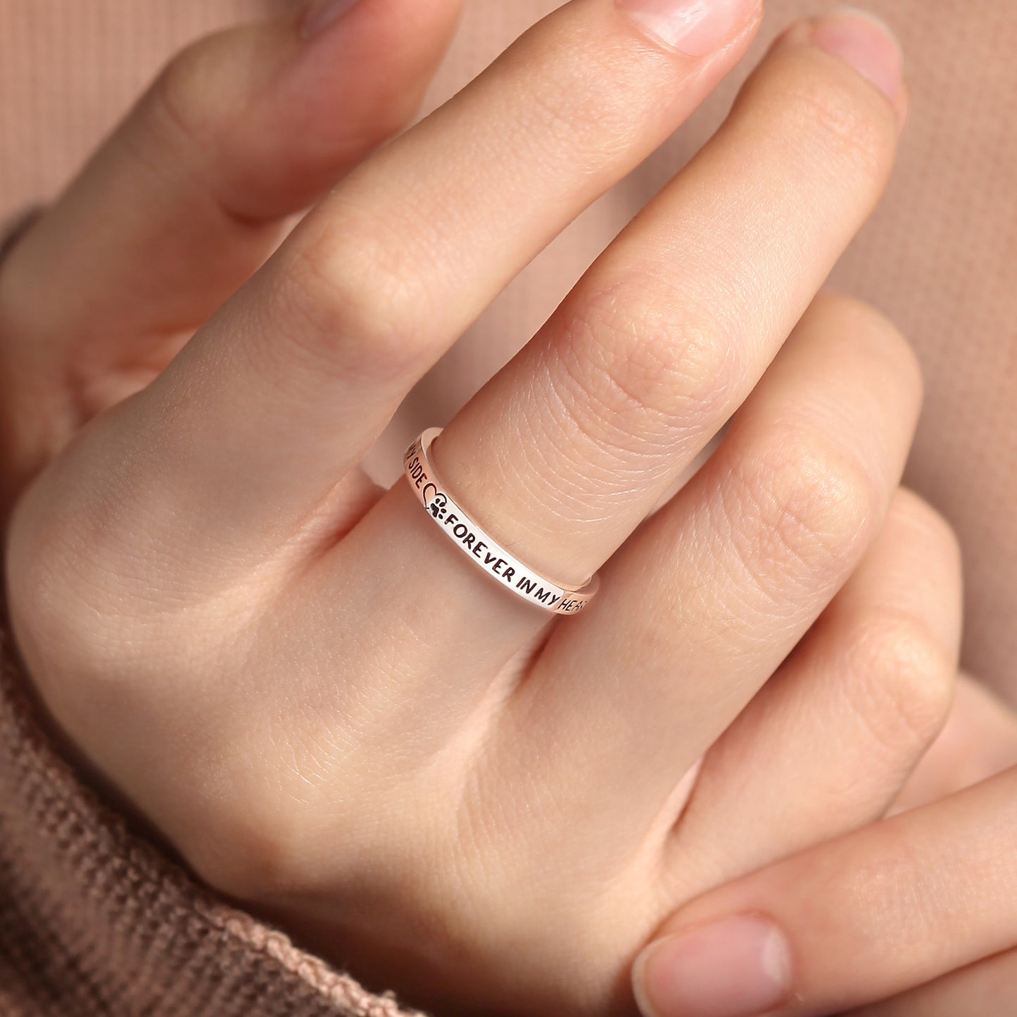 Silver ring with engraved text on a person's finger against a neutral background