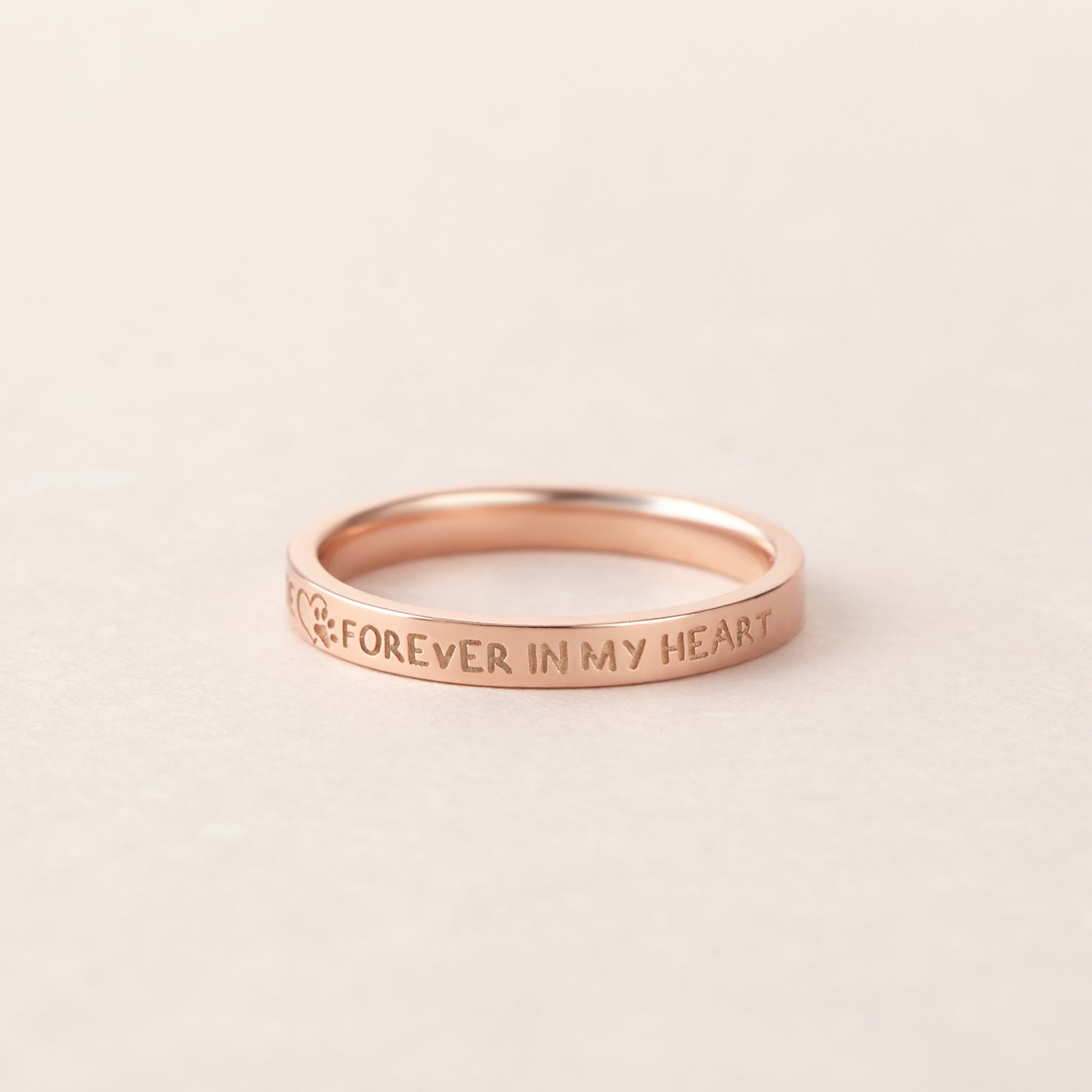 Rose gold ring with 'Forever in My Heart' engraving on a light beige background