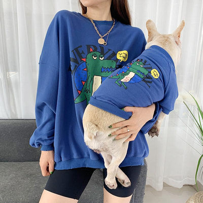 Person wearing a blue sweatshirt with a cartoon design, holding a small dog in a matching blue sweater.