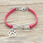 Pink bracelet with silver paw charm and 'love' inscription on a wooden surface