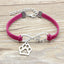 Pink bracelet with silver paw charm and 'love' inscription on a wooden surface