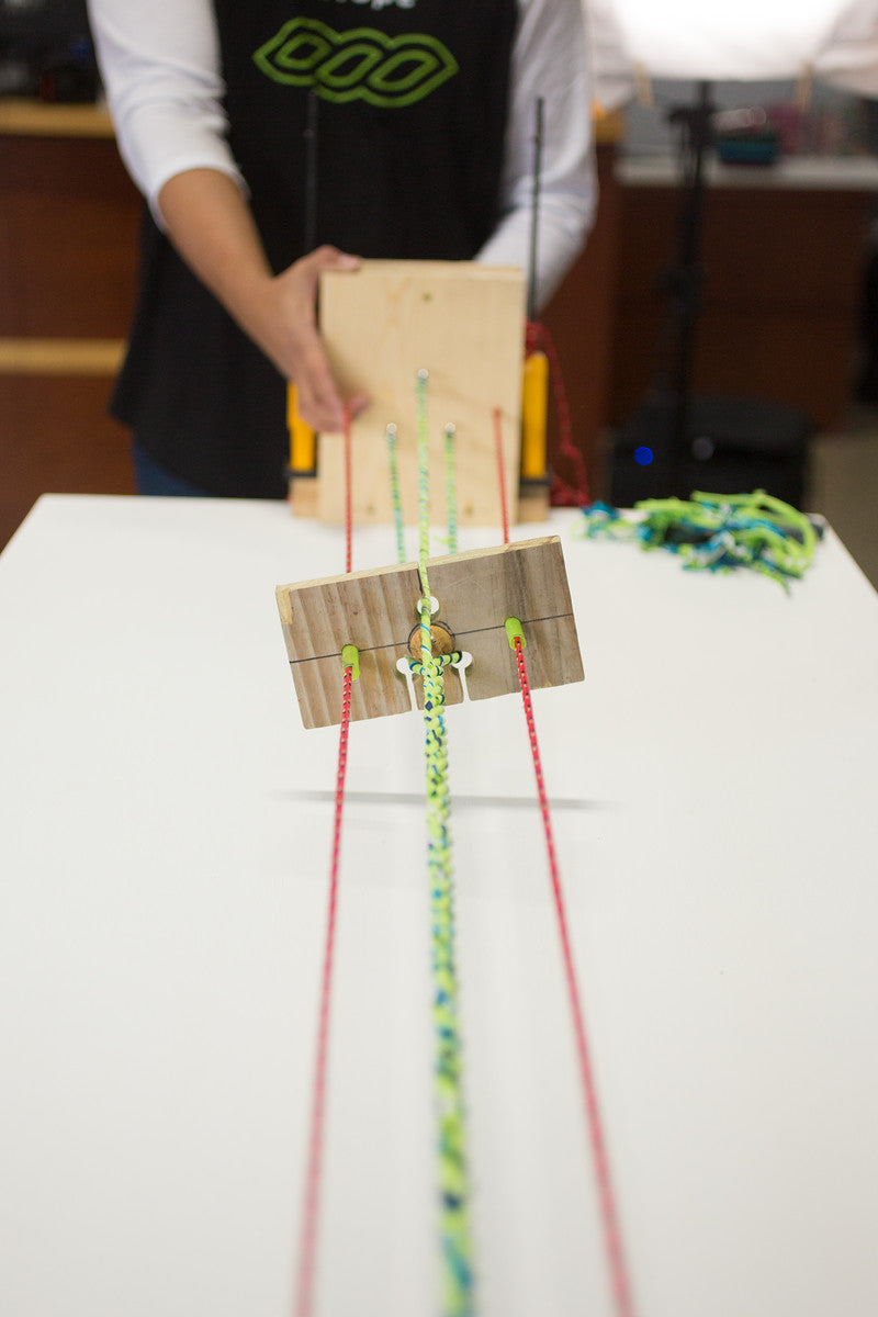 Person holding a wooden loom with colorful strings on a white surface