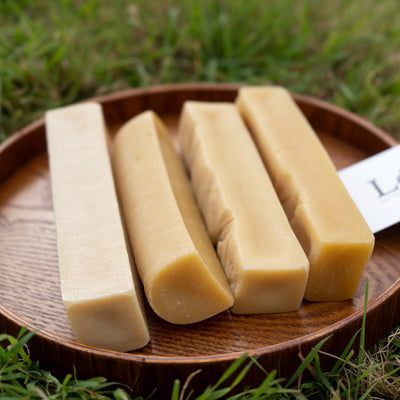 Four bars of soap on a wooden plate with a grassy background