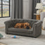 Dog lying on a gray sofa in a living room with curtains and a lamp in the background.