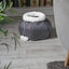 Gray pet bed with white pom-poms on a wooden floor next to a gray armchair.