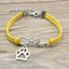 Yellow bracelet with silver paw charm and 'love' inscription on a wooden surface