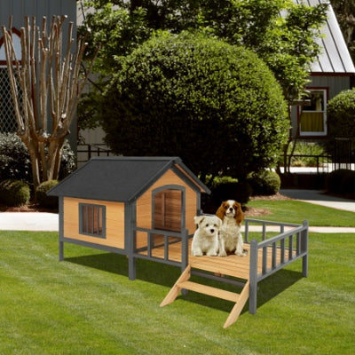 Wooden dog house with a ramp on a grassy area with two dogs.