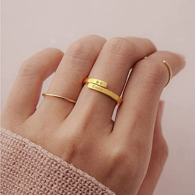 Gold ring with paw print design and engraved text on a hand against a light pink background