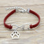 Bracelet with red cord, silver paw charm, and infinity symbol on a wooden surface