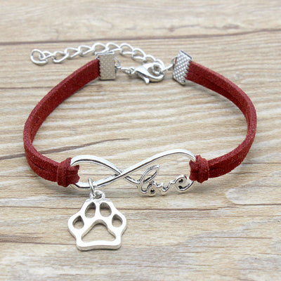 Bracelet with red cord, silver paw charm, and infinity symbol on a wooden surface