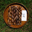 Three braided dog treats on a wooden plate with a 'Lof' brand card on a grassy background