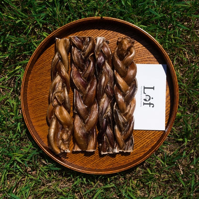 Three braided dog treats on a wooden plate with a 'Lof' brand card on a grassy background