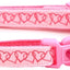 Pink cat collar with heart pattern and decorative ball on a white background