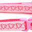 Pink dog collar with heart patterns and a bell charm on a white background