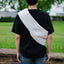 Person wearing a black t-shirt with a white bag slung over one shoulder in an outdoor setting.