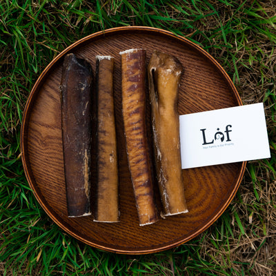 Dog chew bones on a wooden plate with a 'Lof' brand card on grass
