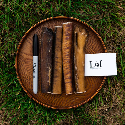 Wooden plate with dog bones and a pen on grass, featuring the brand 'Láf'.