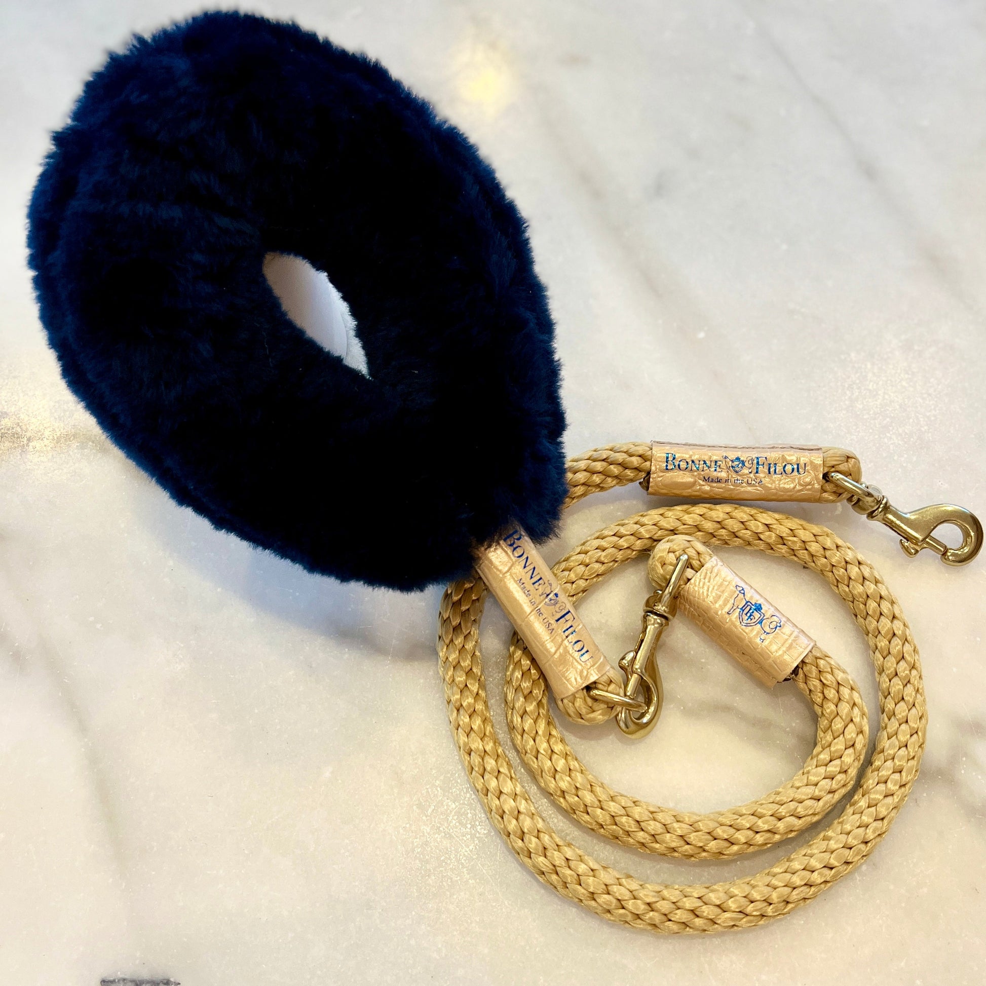Navy blue fur dog muzzle with a gold braided leash on a white surface
