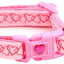Pink dog collar with heart patterns and a matching bell on a white background