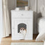 White wooden pet house with a cat peeking out, placed on a wooden floor in a room.