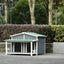 Gray outdoor dog house with green roof in a garden setting