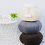 Stack of three round cushions in beige, gray, and brown on a white surface with a small plant and books in the background.