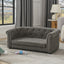 Gray tufted sofa in a living room with curtains and a lamp in the background.